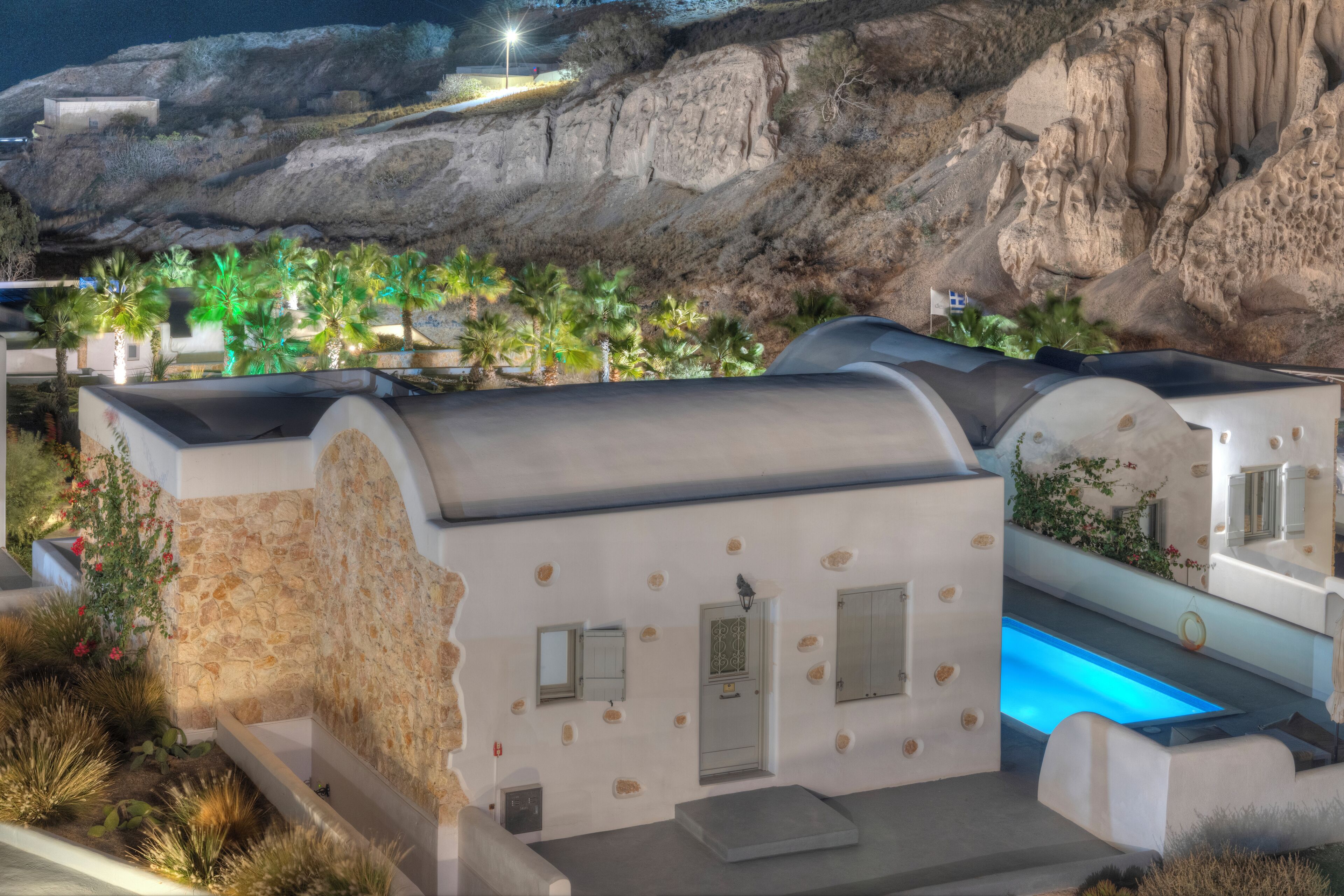 A modern building with a pool, stone walls, and a rocky hillside backdrop.