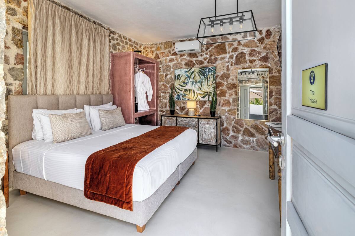 Ein Schlafzimmer mit Steinwand, einem Bett mit weißer Bettwäsche, einem Holzregal mit aufgehängtem Bademantel, einem Gemälde und einem Schild an der Wand.