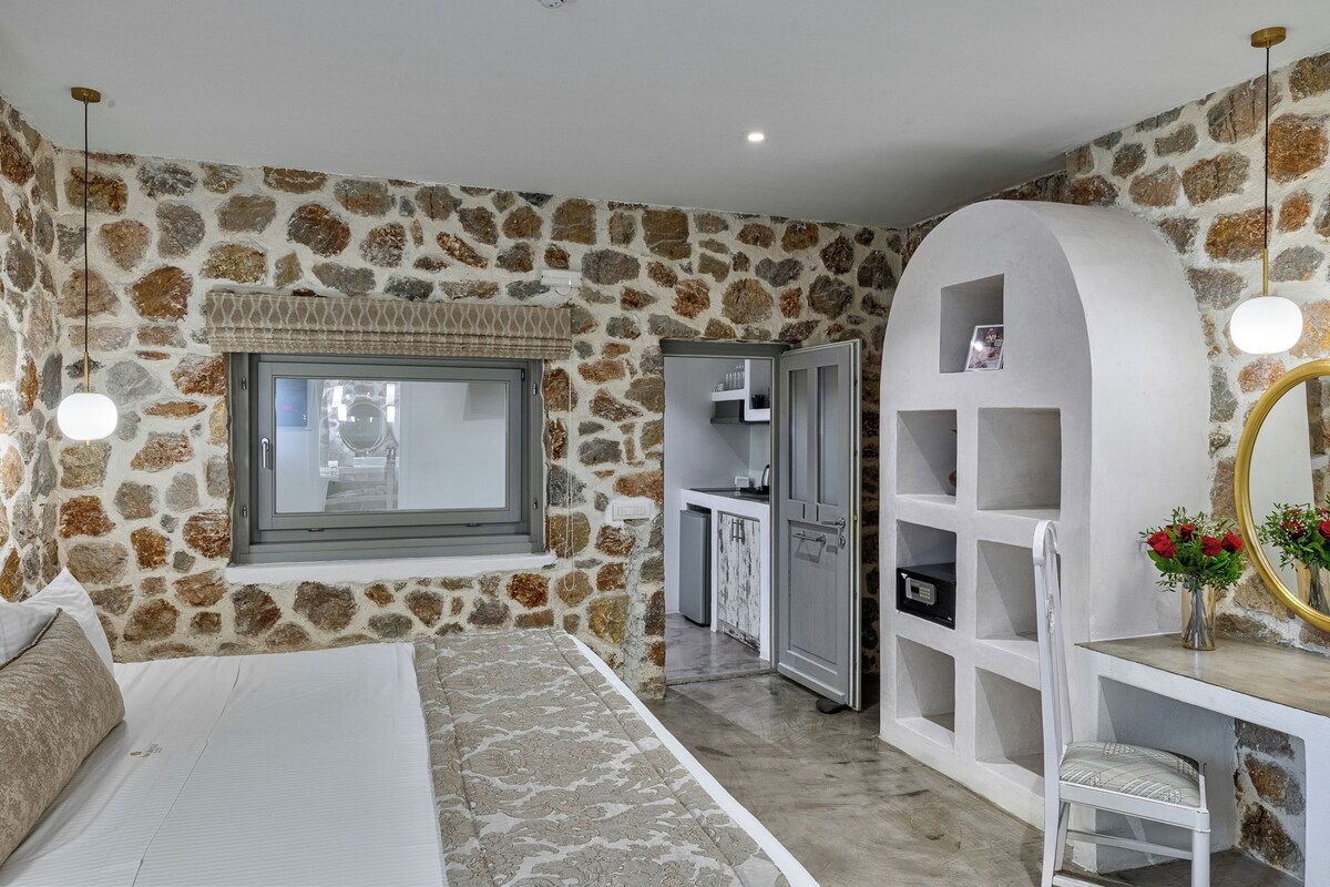 Un dormitorio con pared de piedra, una cama, un escritorio con espejo y una ventana.