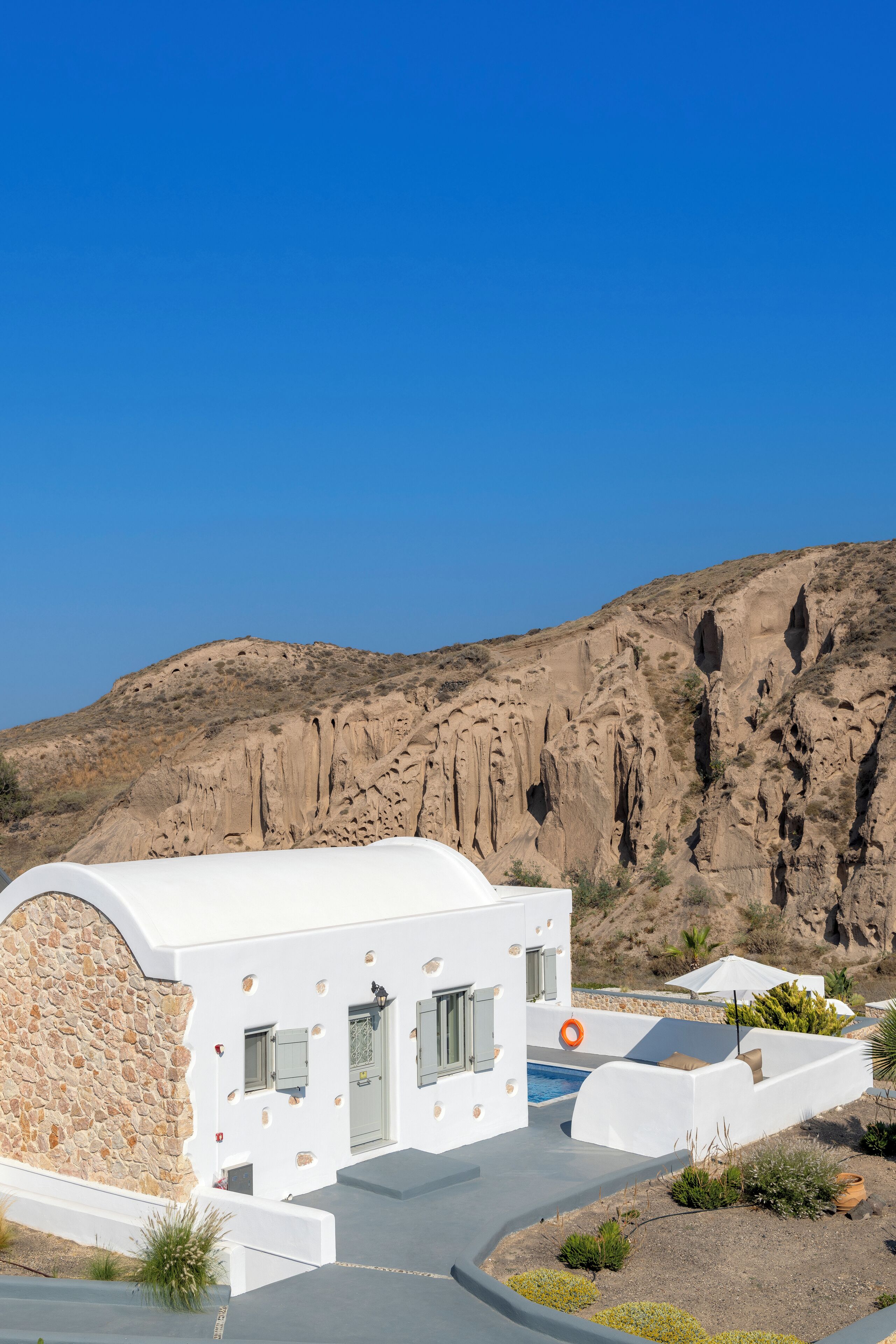 A modern white building with a stone facade, a pool, and a mountainous backdrop.