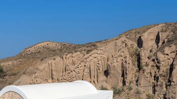A modern white building with a stone facade, a pool, and a mountainous backdrop.