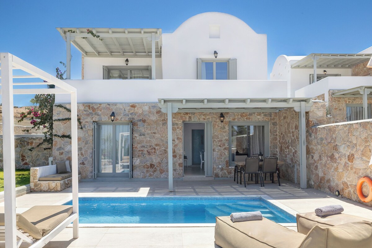 Una villa moderna con piscina, muros de piedra y un patio cubierto.