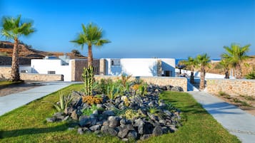Un edificio moderno con fachada blanca, rodeado de un jardín cuidado con rocas y palmeras.