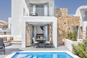 A modern two-story building with a pool, outdoor seating, and a stone wall. - Desiterra Resort & Spa (Santorini)