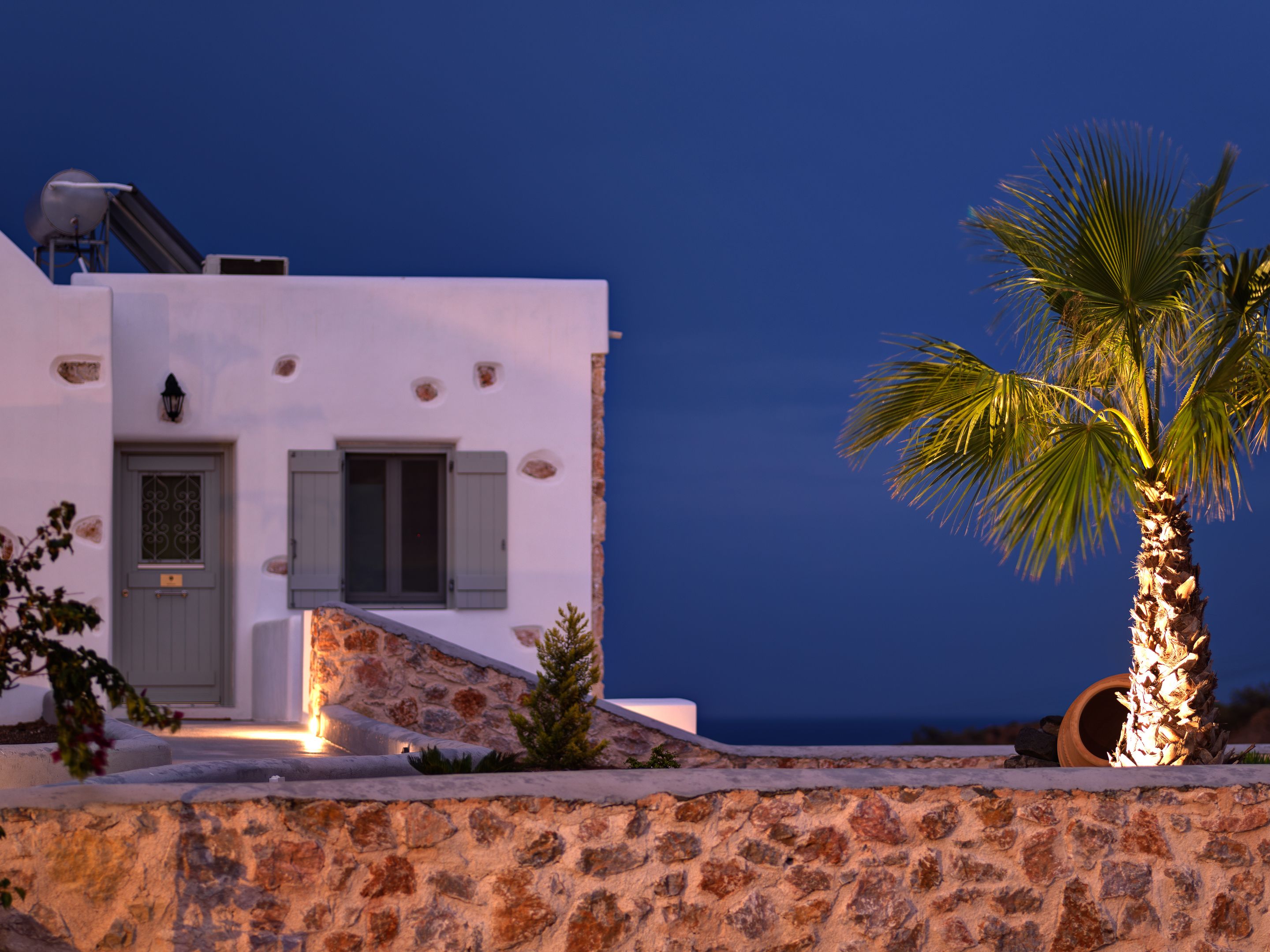 A white building with a stone wall, a door, and shutters.
