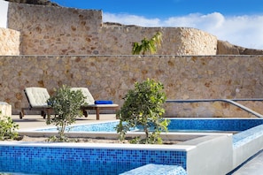 A stone wall with a pool and lounge chairs. - Desiterra Resort & Spa (Santorini)