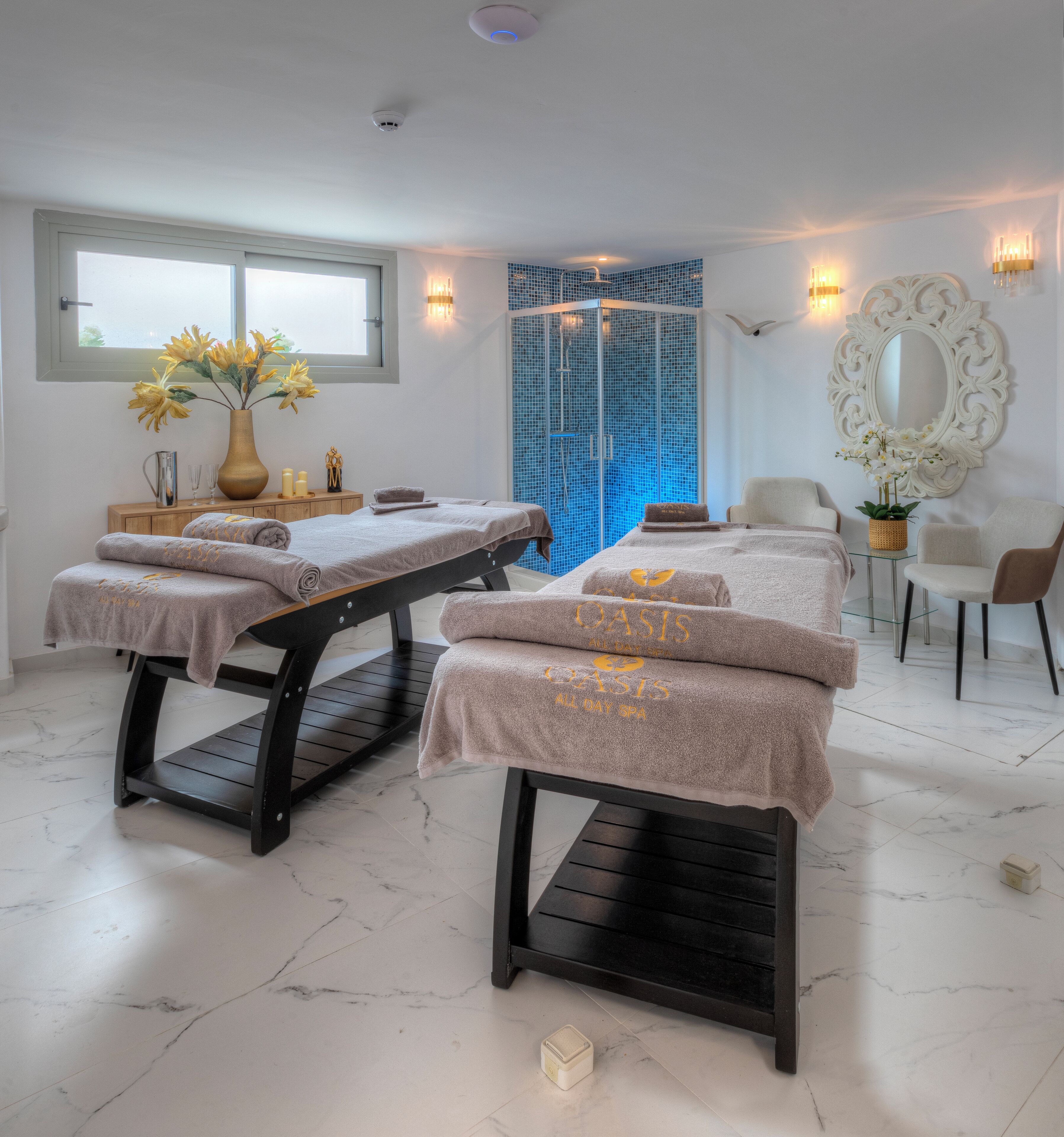 A spa room with two massage tables, a large mirror, and a blue shower enclosure.