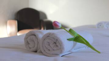 Una cama bien hecha con toallas blancas enrolladas y una sola tulipa rosa.