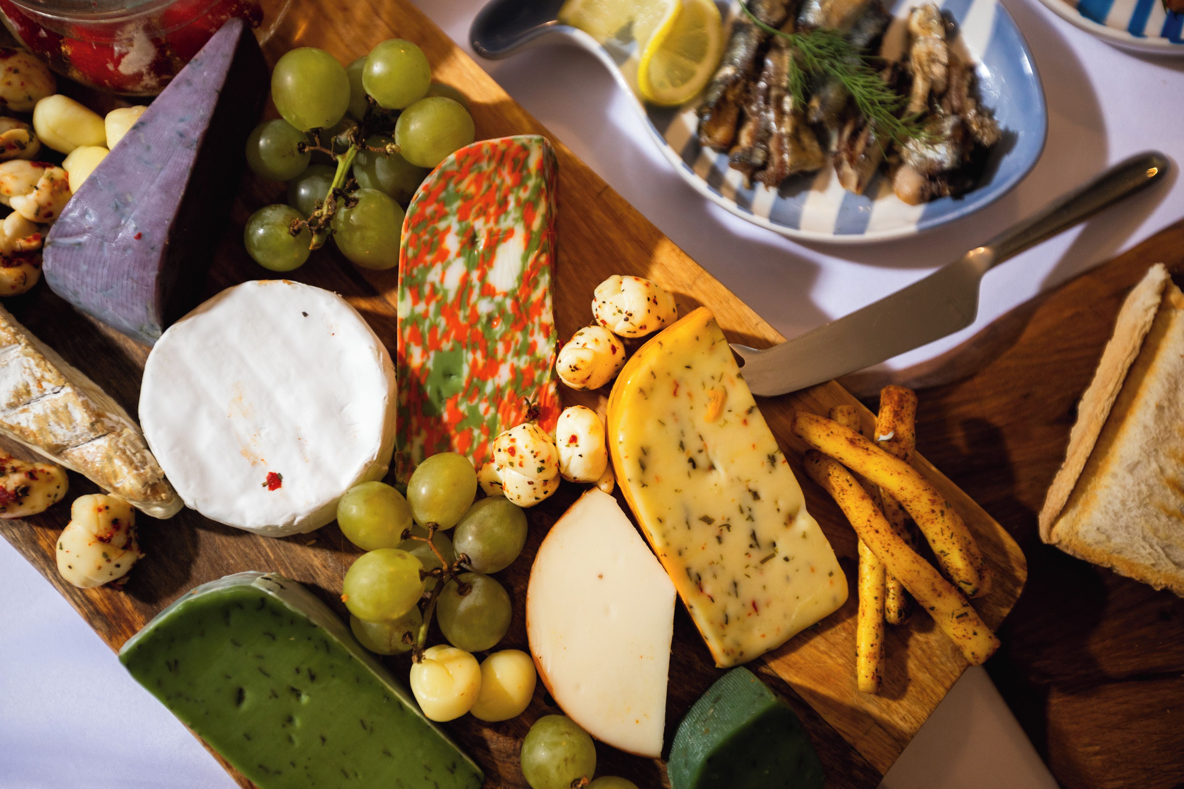 A variety of cheeses, grapes, and bread on a wooden board.