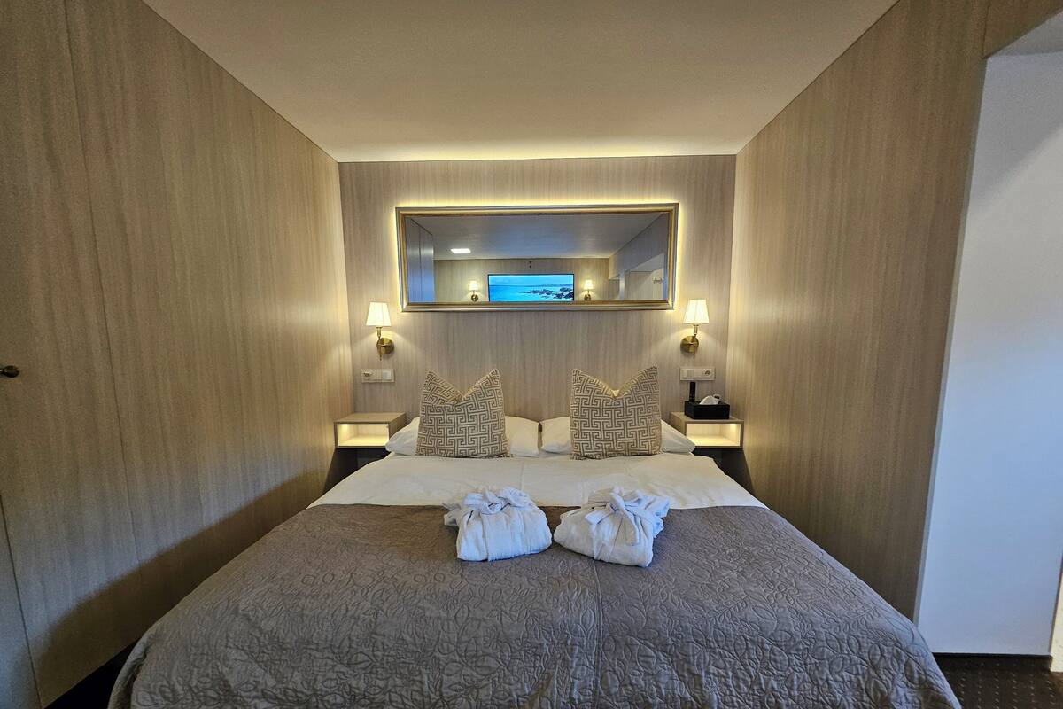 A hotel room with a large bed, two nightstands, a wall-mounted TV, and a mirror above the bed.