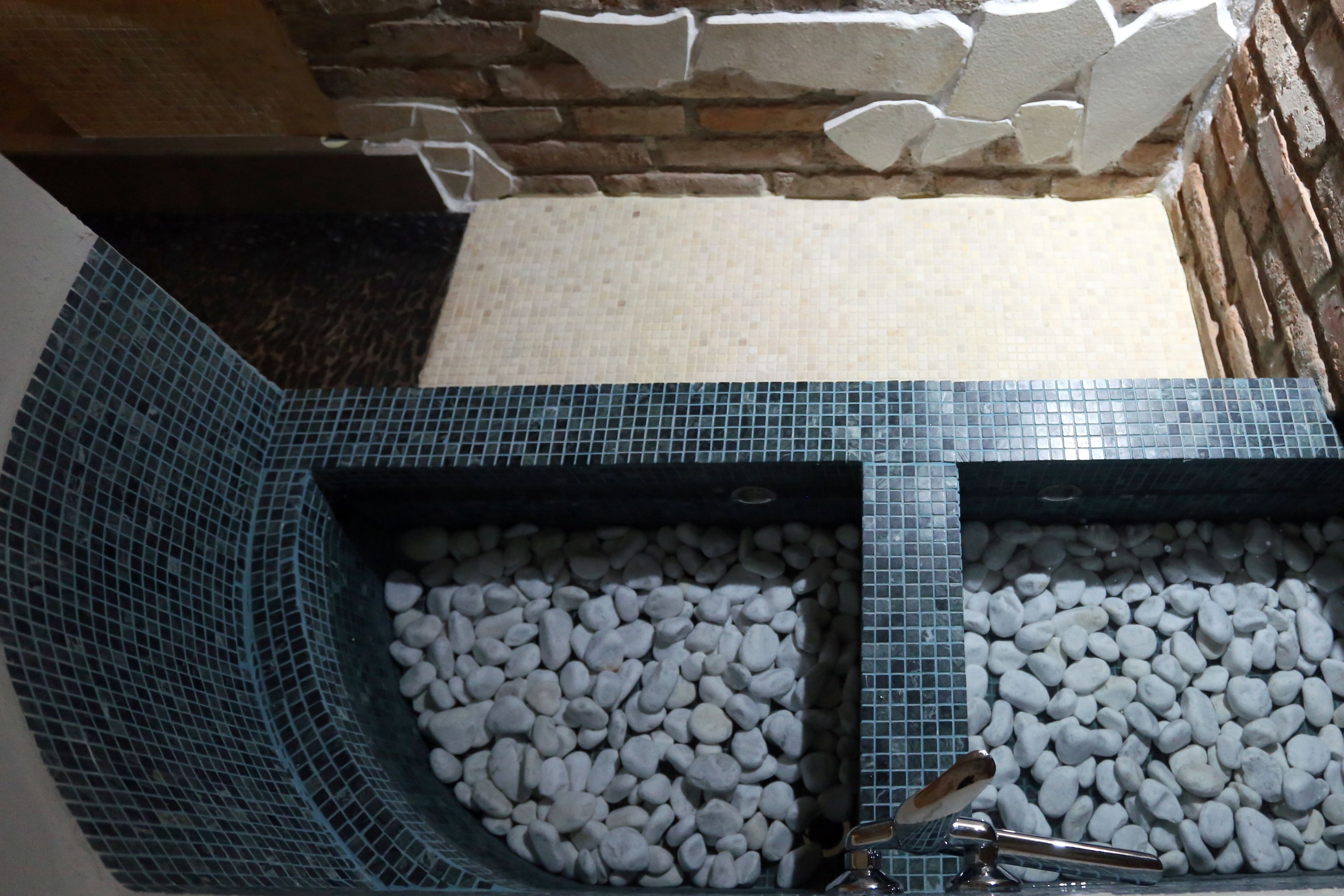 Un baño con piso de baldosas, pared de piedra y una bañera llena de guijarros blancos.
