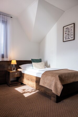 A hotel room with a bed, a nightstand, a lamp, a window with curtains, and a wall-mounted picture. - Penzión & Wellness Zoborská (Nitra)