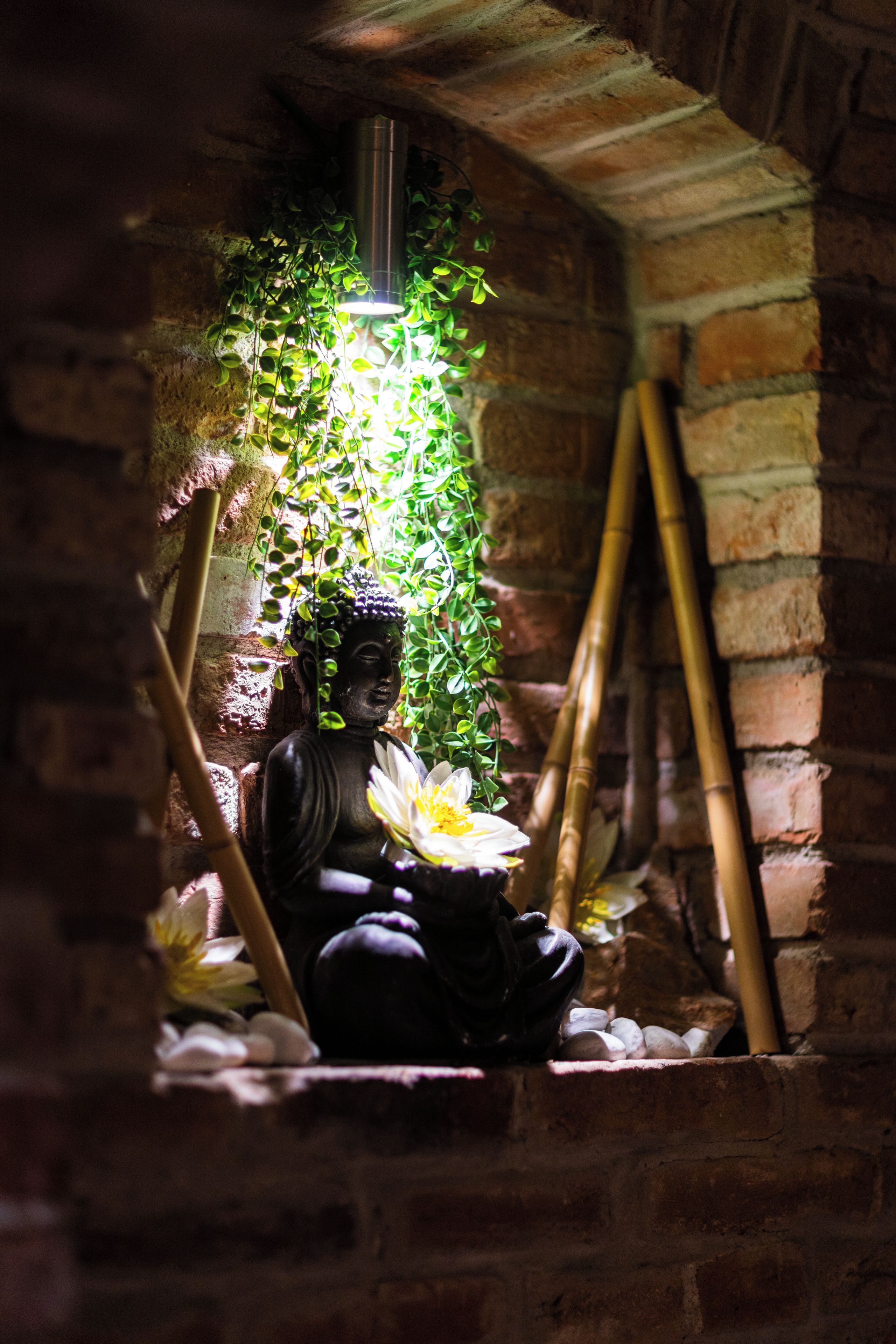 A statue of a seated figure with a lotus flower, surrounded by greenery and bamboo.