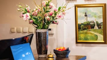 A reception desk with a vase of flowers, a painting, and a fruit bowl.