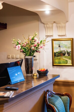 A reception desk with a vase of flowers, a painting, and a fruit bowl. - Penzión & Wellness Zoborská (Nitra)