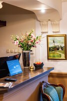 A reception desk with a vase of flowers, a painting, and a fruit bowl.