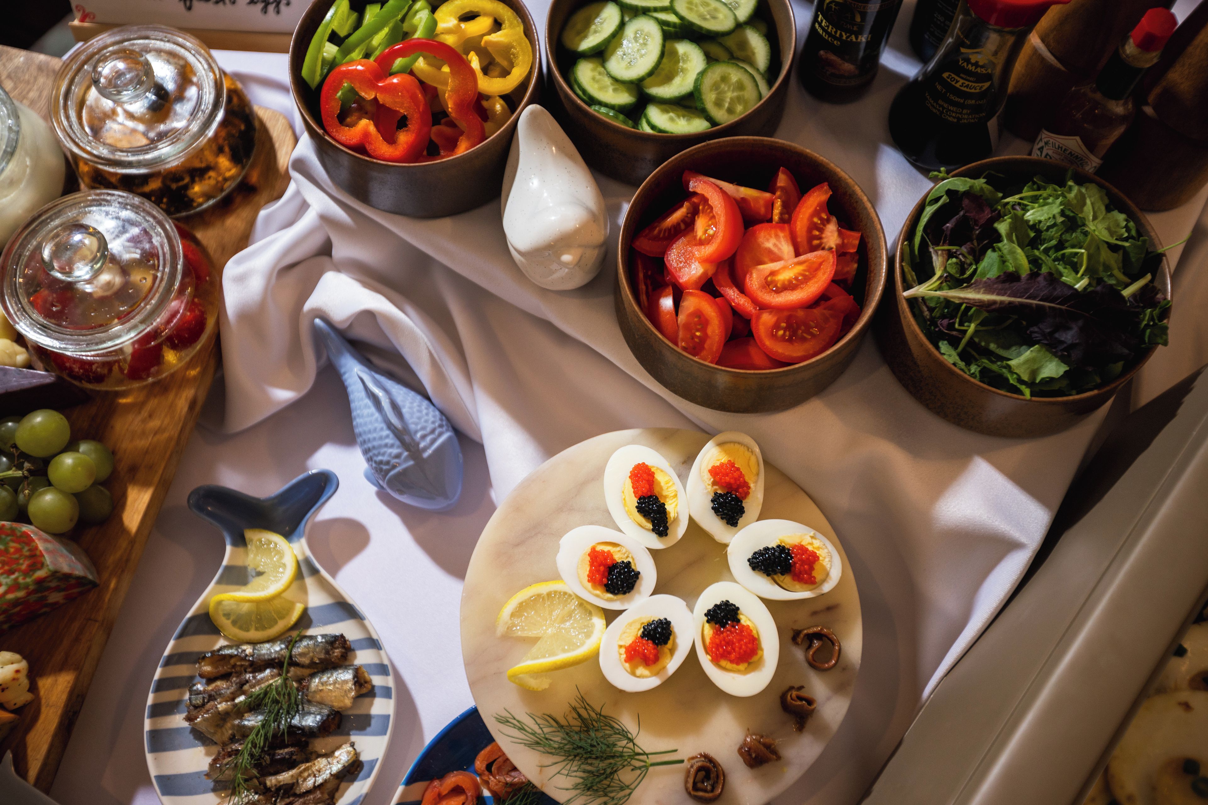 Une table sur laquelle on trouve divers aliments, notamment des légumes coupés en tranches, un saladier de tomates et une assiette d’œufs mimosa garnis de caviar.