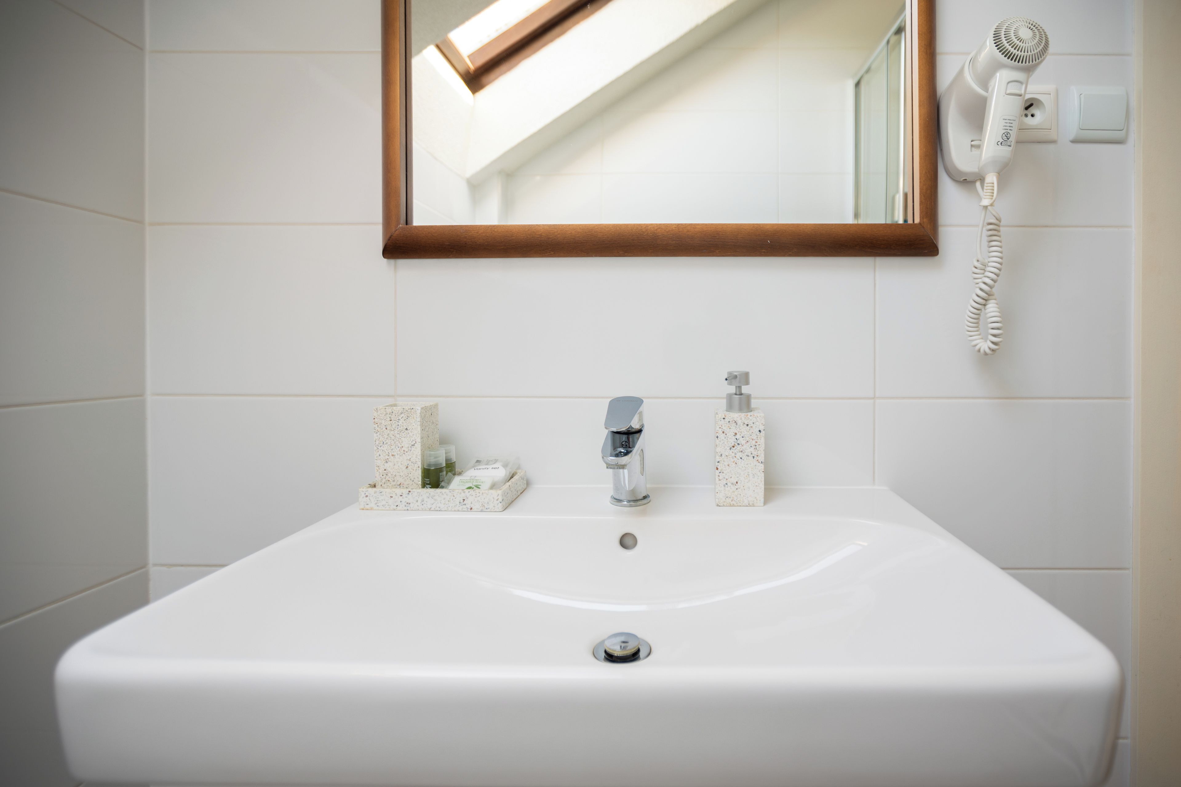 A bathroom with a white sink, a mirror with a wooden frame, and a hairdryer on the wall.