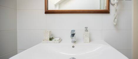 A bathroom with a white sink, a mirror with a wooden frame, and a hairdryer on the wall.