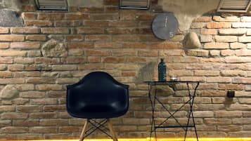 A room with a brick wall, a black chair, a small table with a bottle, and a clock.