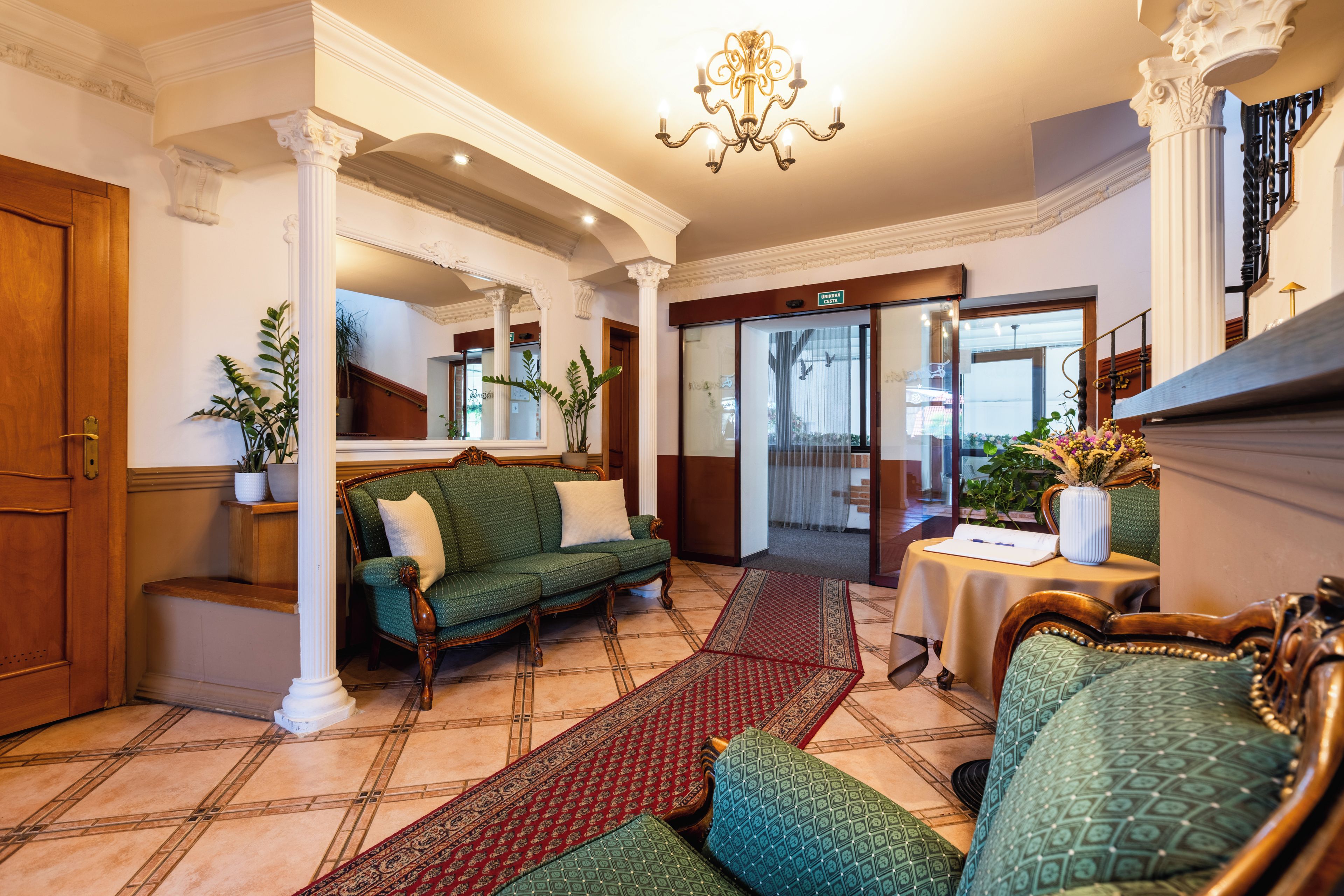 Un vestíbulo de hotel con un sofá verde, una mesa de madera con un jarrón y una araña.