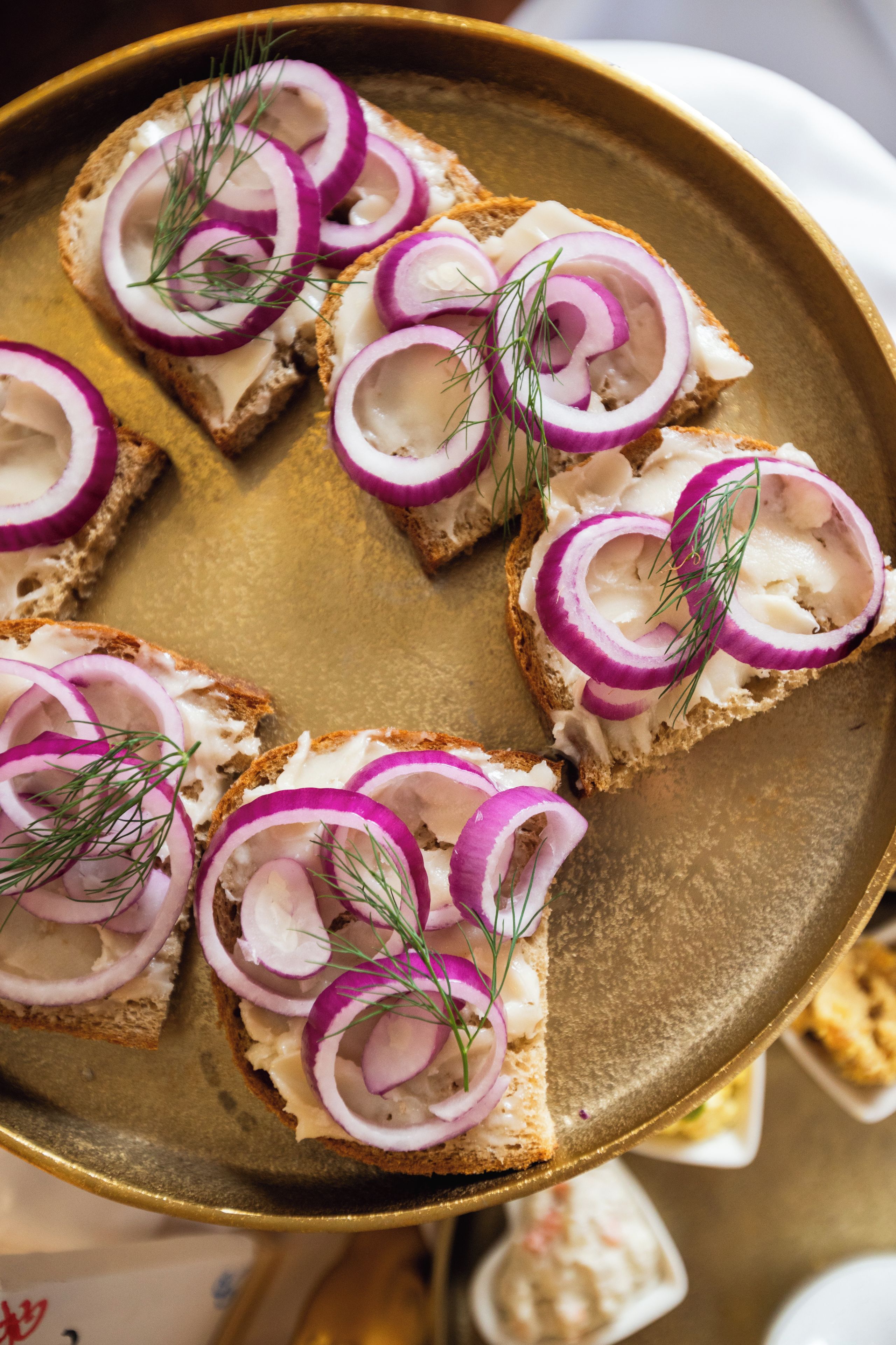 A tray with several pieces of bread topped with cream cheese, red onion slices, and dill.