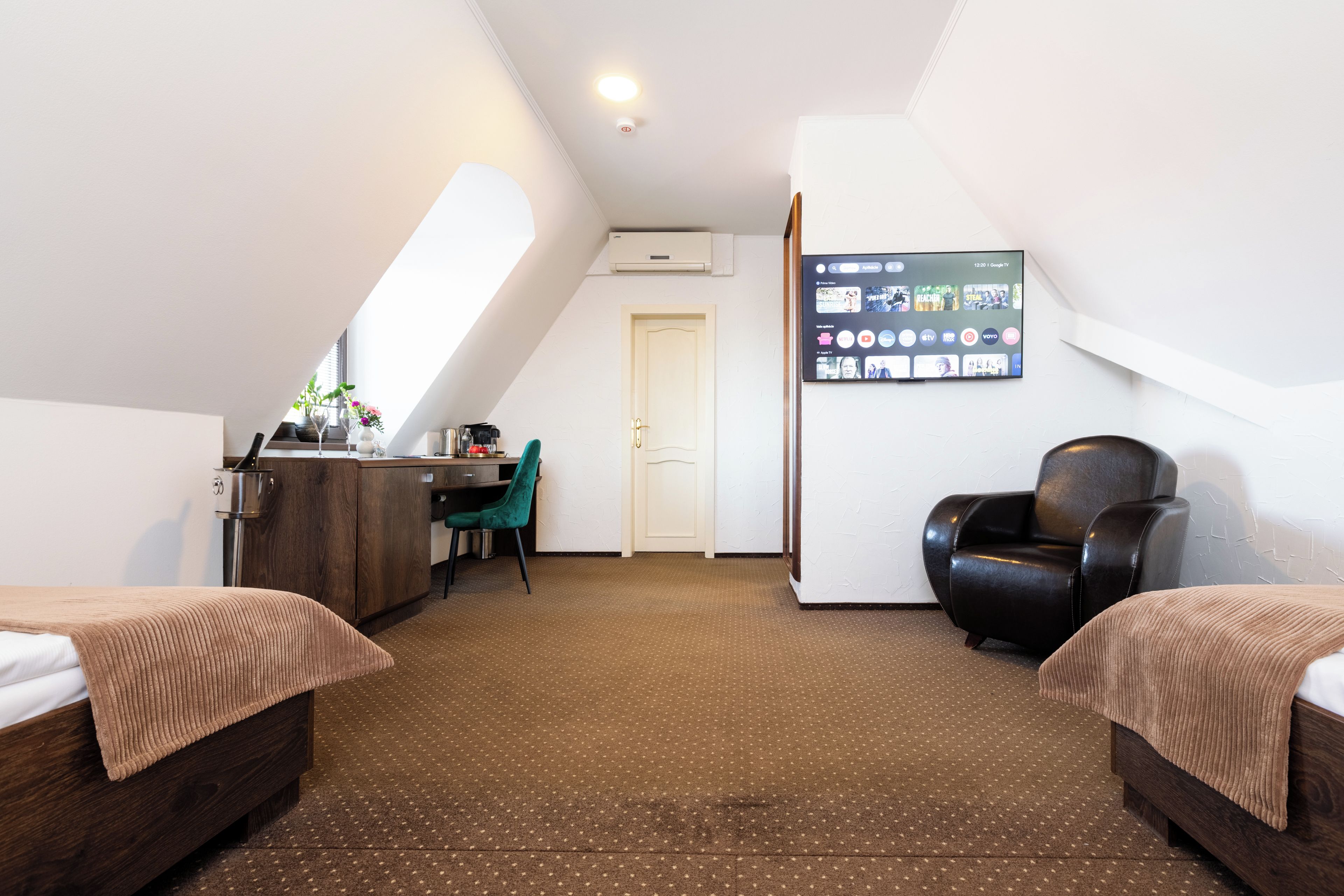A room with two beds, a desk, a chair, and a TV mounted on the wall.