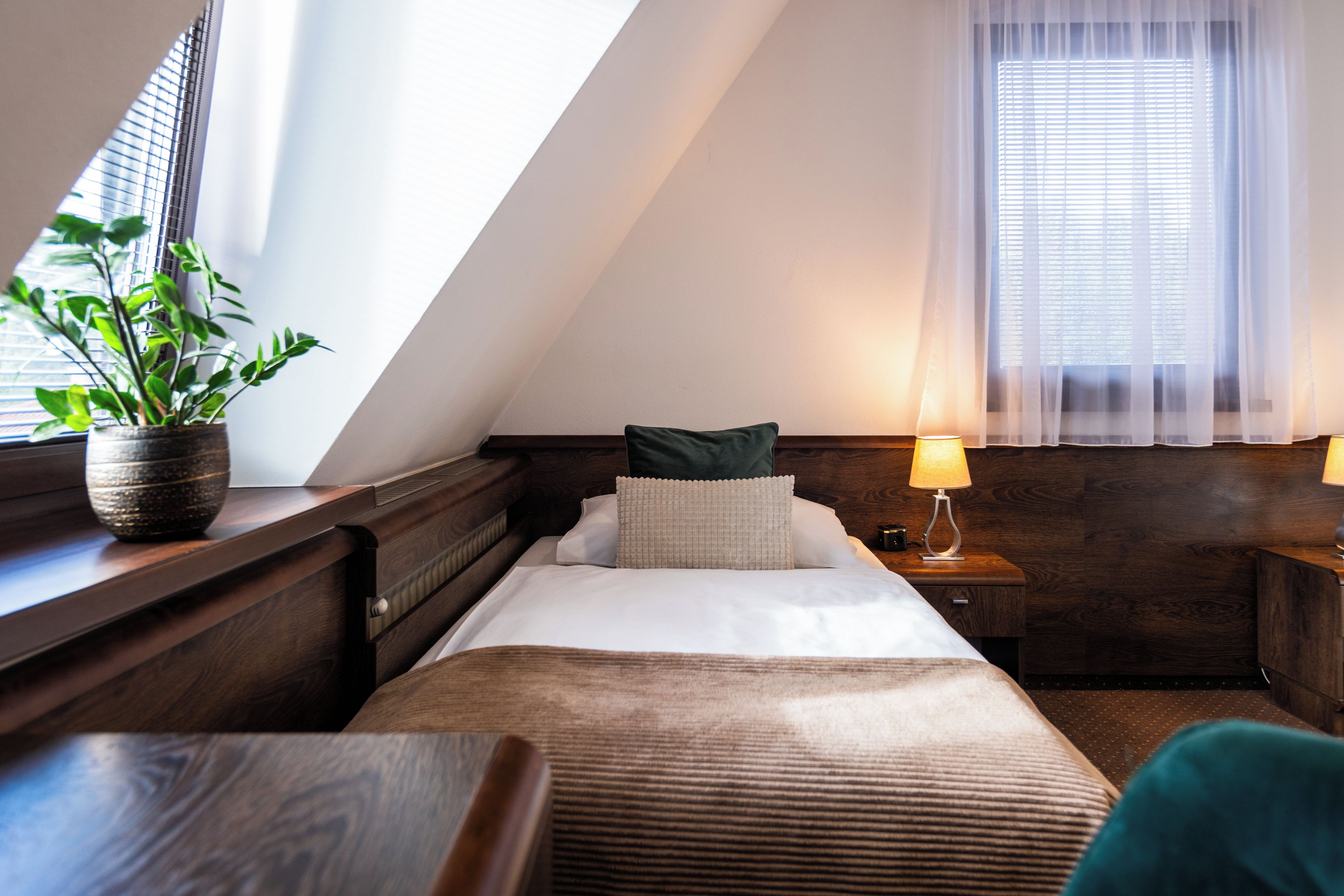 Un dormitorio con cama, mesitas de noche, lámpara, planta en maceta y ventana con persianas.
