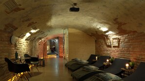 A cozy, dimly lit room with brick walls, a wooden ceiling, and a small table with chairs. There are several cushioned seating areas with pillows and a lit candle. - Penzión & Wellness Zoborská (Nitra)