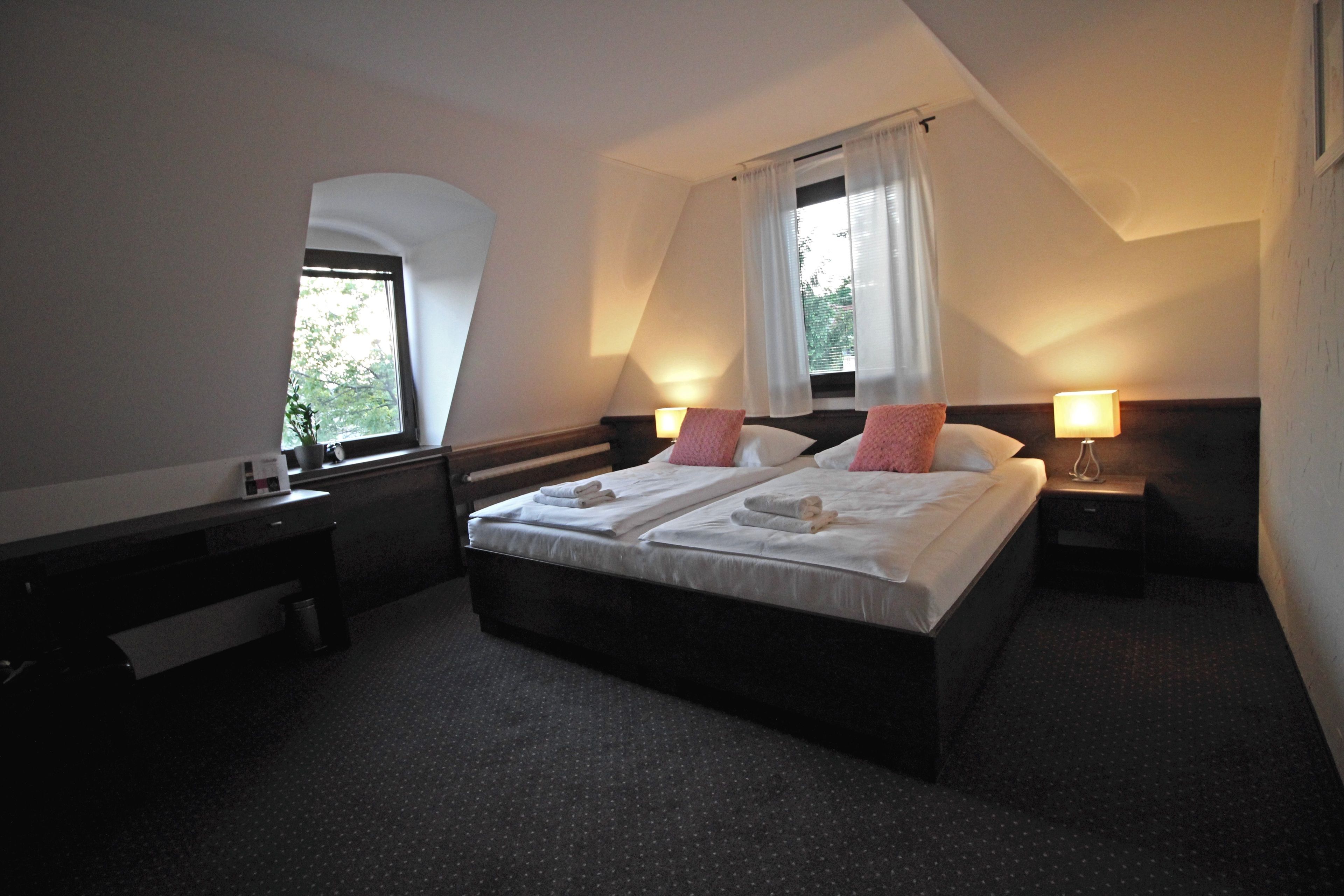A hotel room with a large bed, two bedside tables, a nightstand, a window with curtains, and a small desk with a chair.