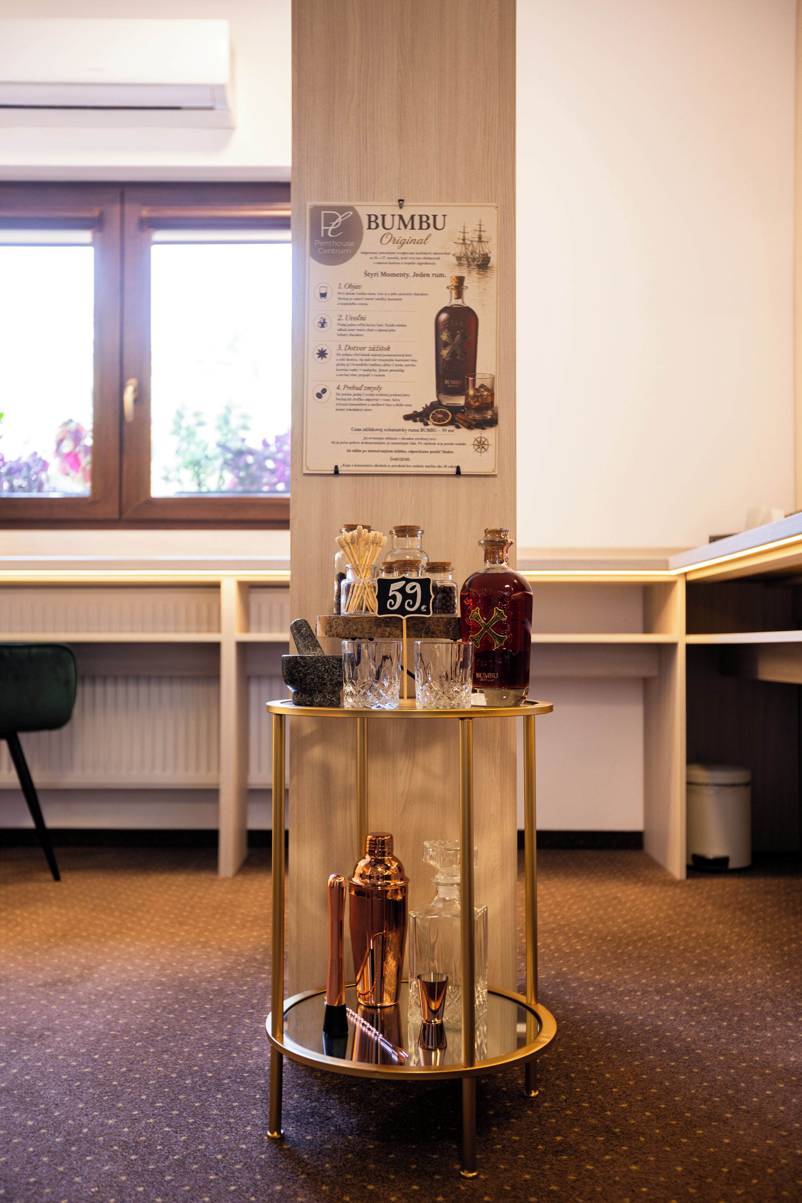 Zona de bar con un cartel de BUMBU Original, un taburete con una botella de BUMBU, un vaso y un shaker de cócteles.