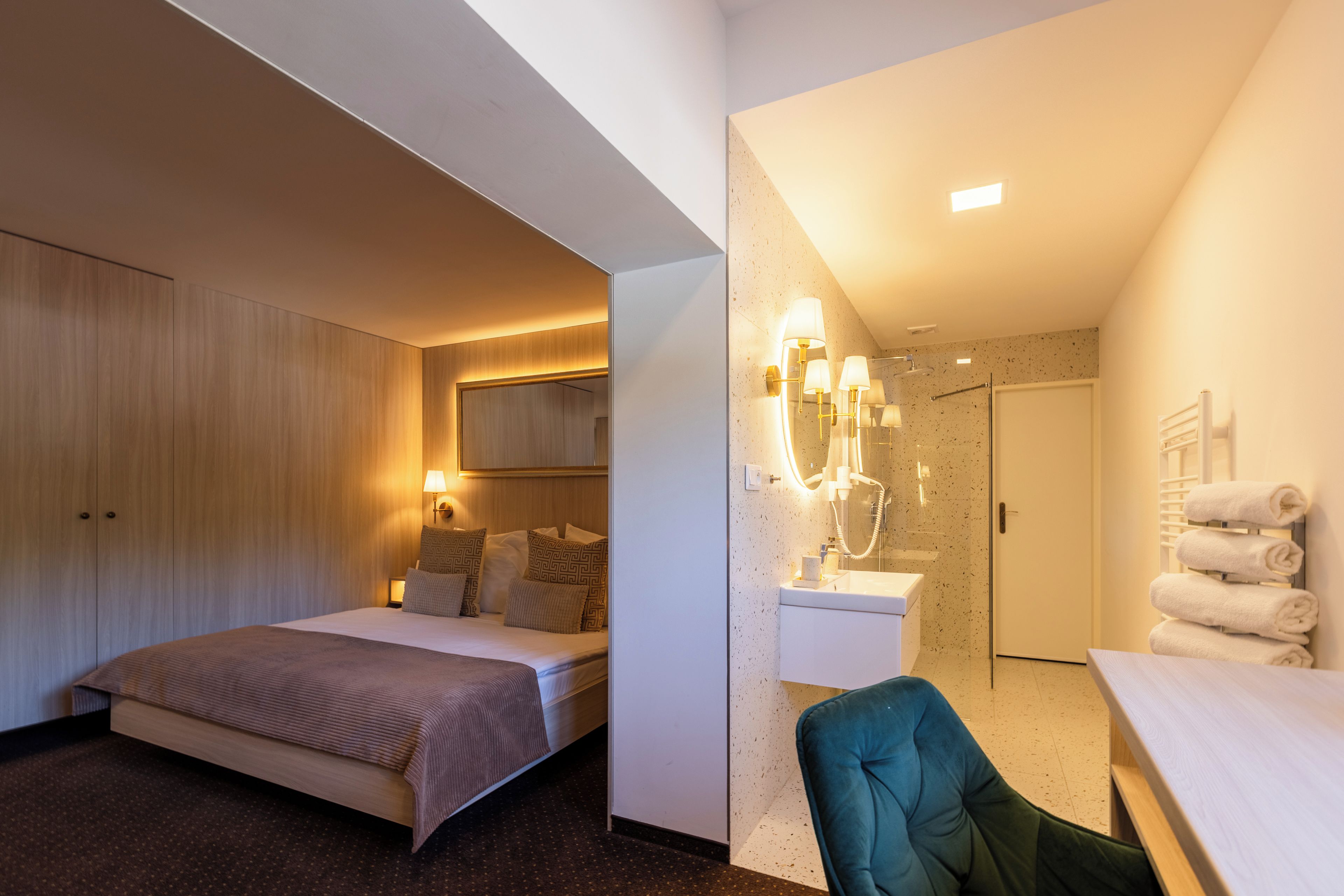 Habitación de hotel con cama, escritorio, silla, baño con ducha y toallero.