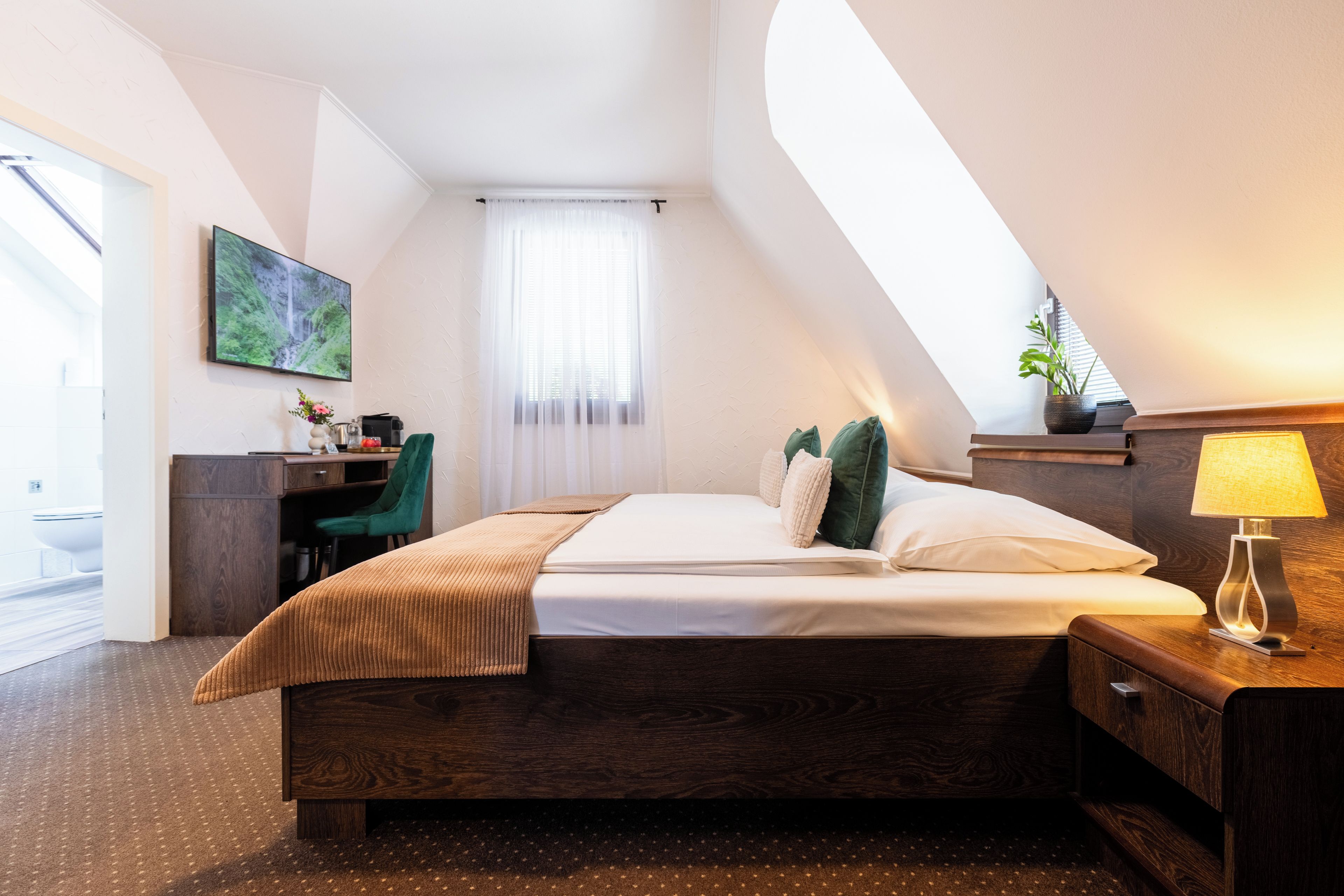 A hotel room with a bed, a desk, a chair, a lamp, and a window with curtains.
