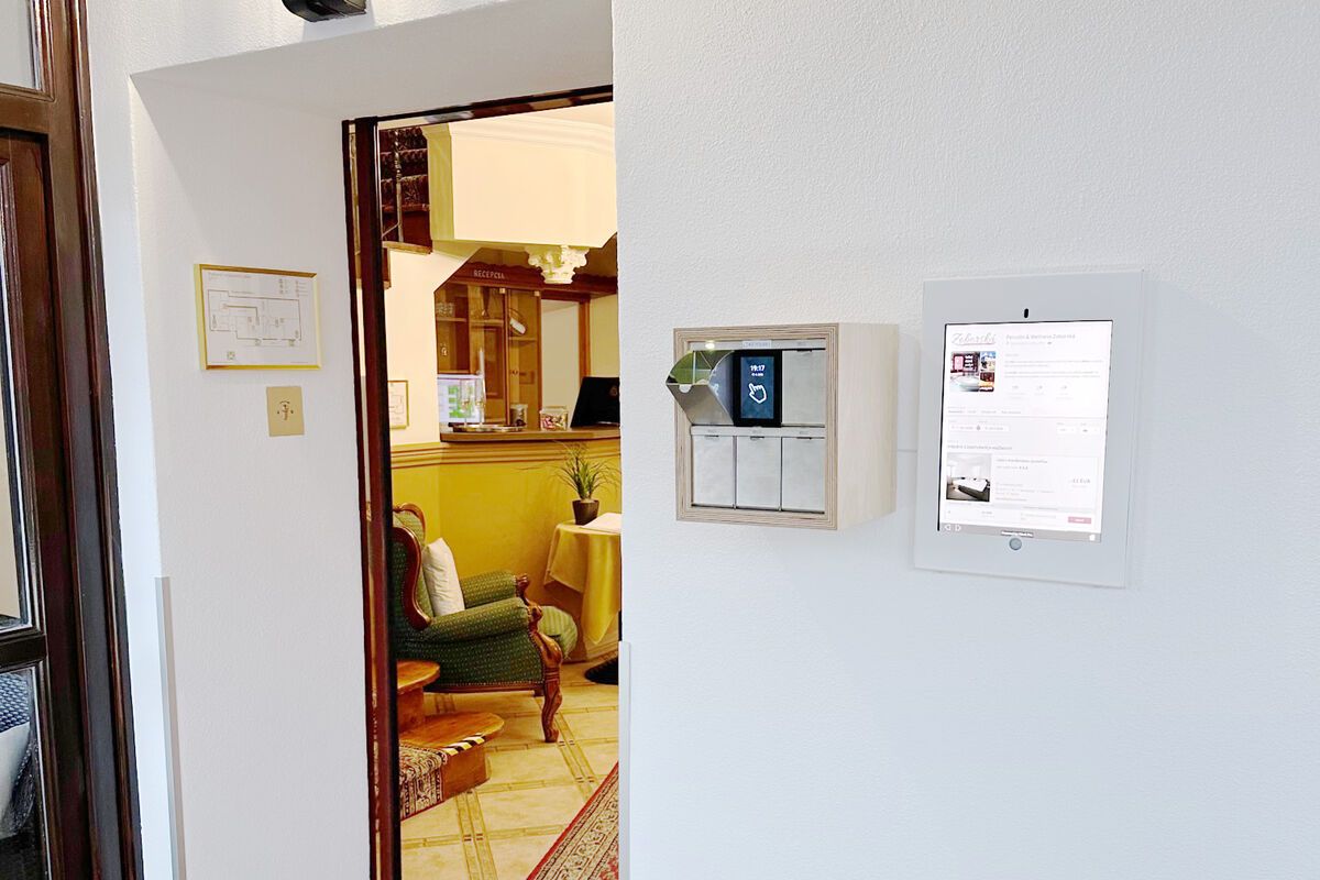 A room with a wooden door, a green armchair, a small table, and a wall-mounted thermostat.