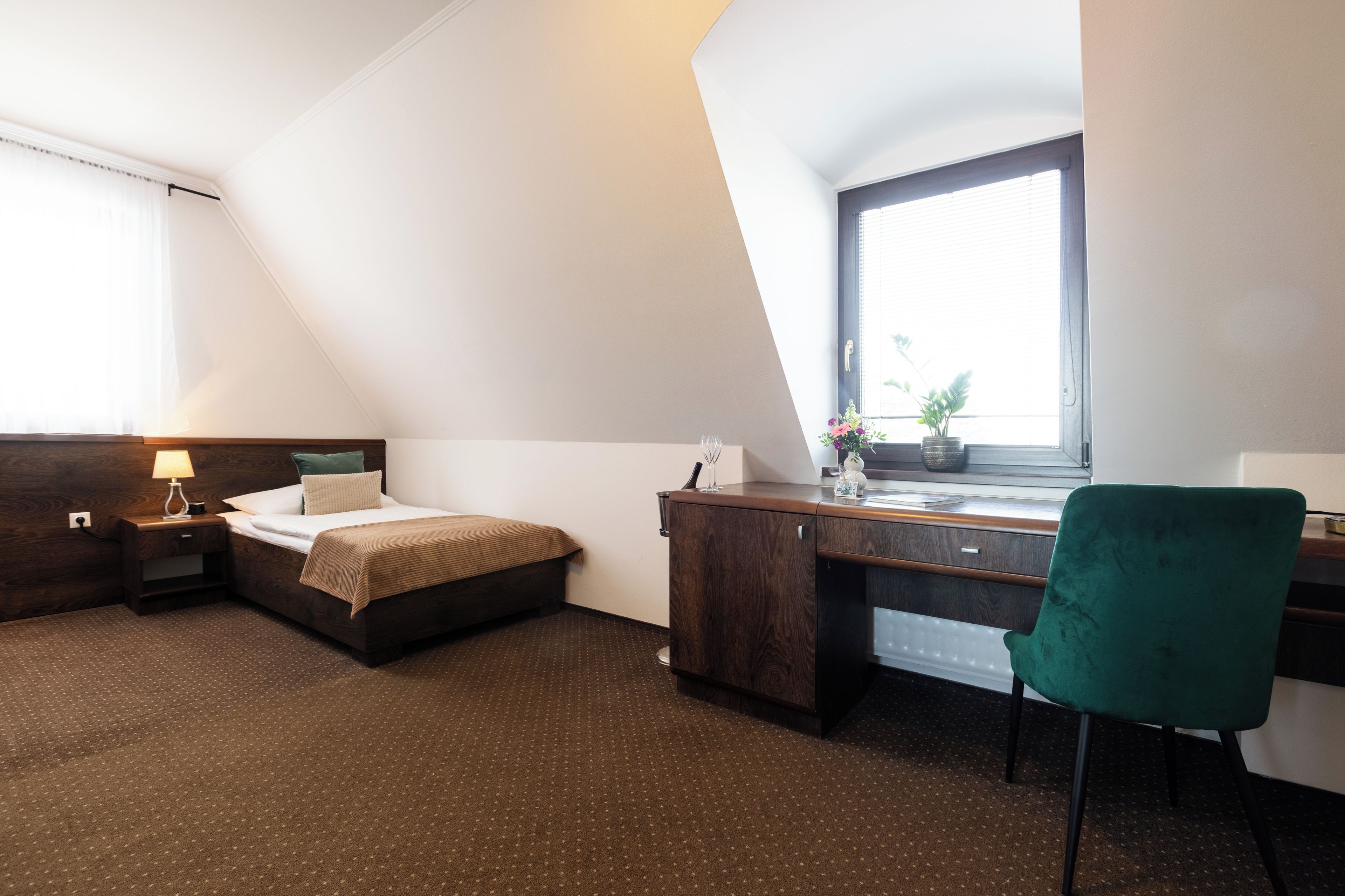 Una camera d'albergo con un letto, una scrivania, una sedia, una finestra e un comodino.