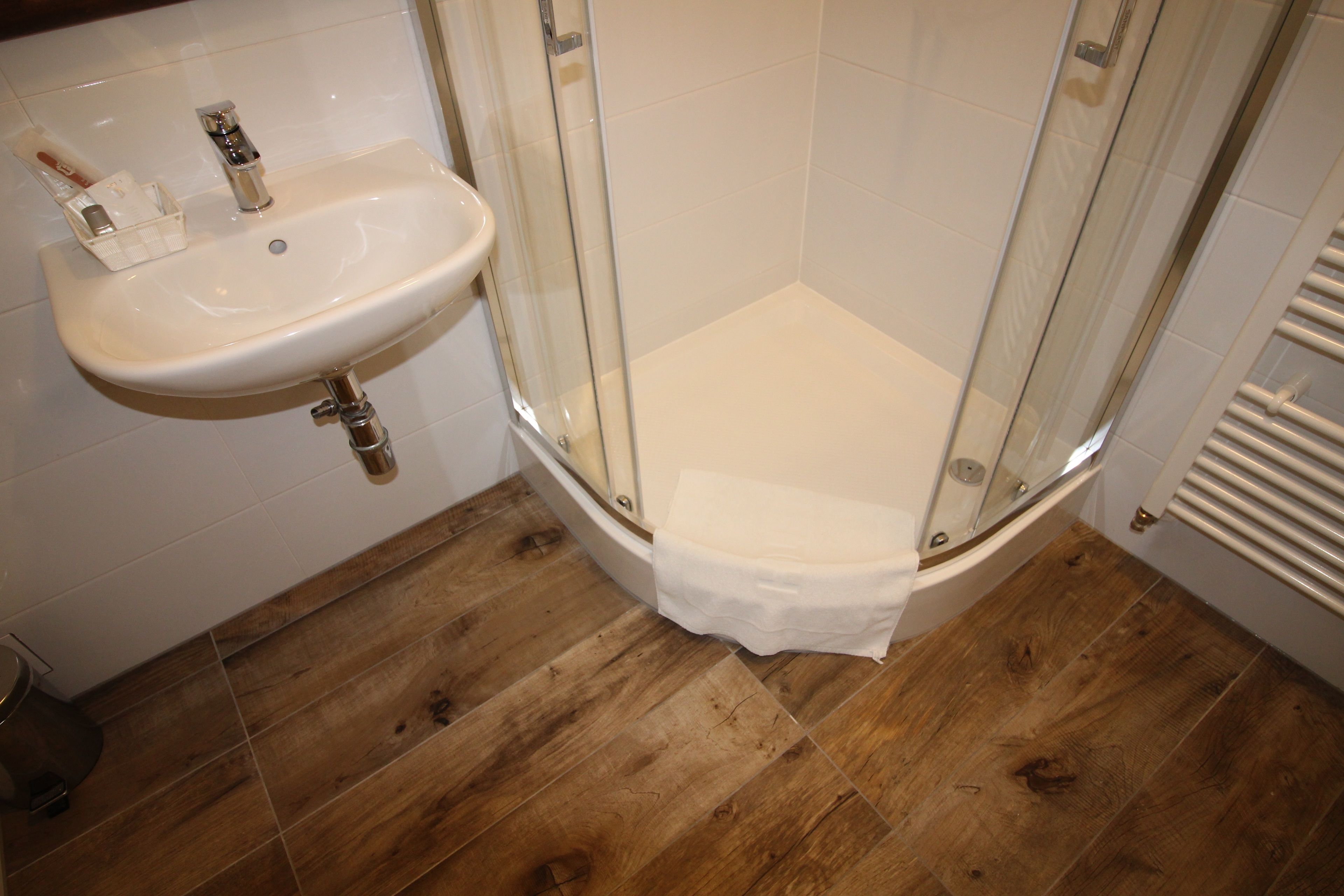 A bathroom with a glass-enclosed shower, a white sink with toiletries, and wooden flooring.