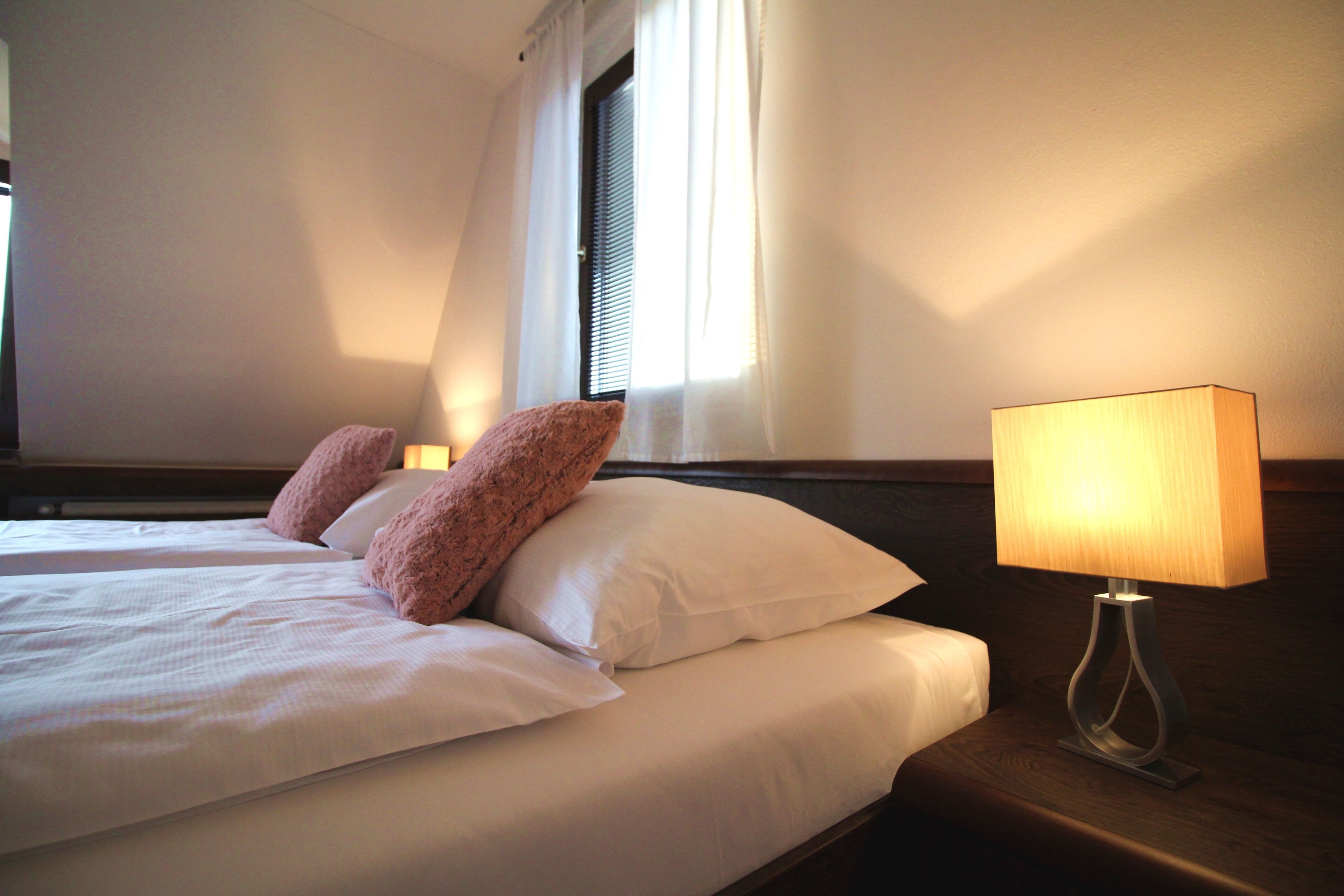 A hotel room with a bed, pillows, a nightstand, and a lamp.