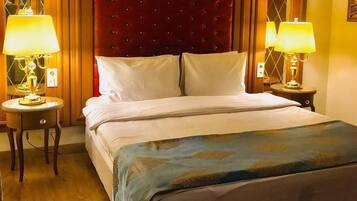 Una habitación de hotel con una cama grande, dos lámparas de noche, un cabecero tapizado en rojo y suelo de madera.