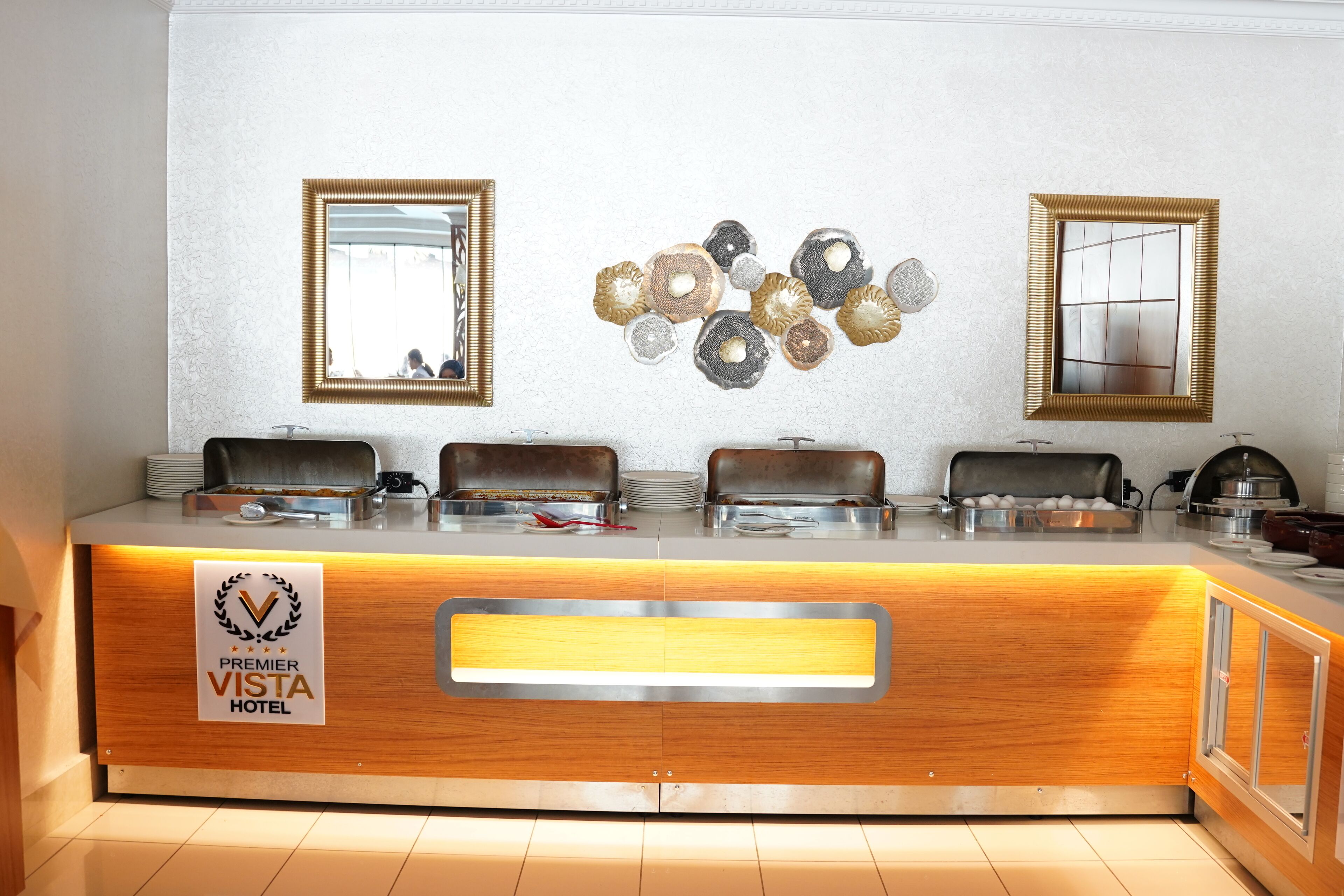 A buffet counter at the Premier Vista Hotel with a wooden finish, two wall-mounted mirrors, and a decorative wall piece.