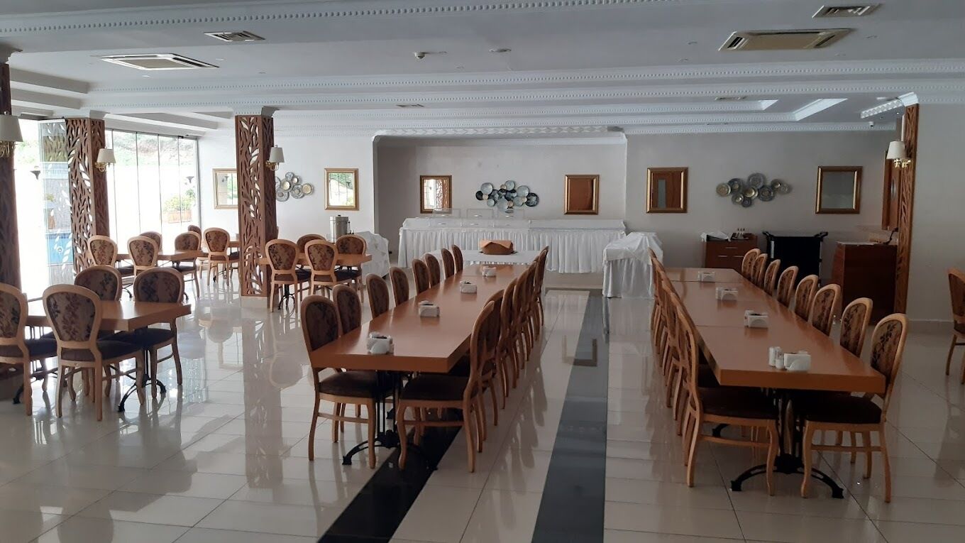 Un vaste espace dédié à la salle à manger, avec de longues tables et des chaises, un sol carrelé et des éléments décoratifs sur les murs.