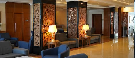 A spacious lobby with modern furniture, including sofas and armchairs, and decorative wooden panels.