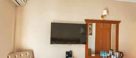 Habitación de hotel con escritorio de madera, dos sillas, un televisor de pantalla plana montado en la pared, minibar y equipo de aire acondicionado.