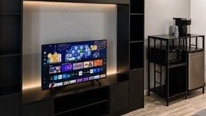 A modern living room with a flat-screen TV, built-in shelving, and a coffee machine. - Lake George Residence LLC (South Glens Falls)