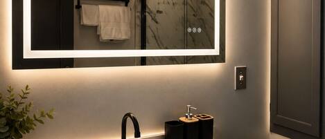 A bathroom with a large mirror, a white sink, dark cabinets, and a towel rack with towels.