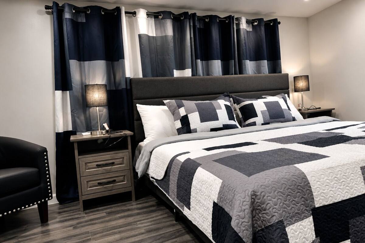 Quarto com cama, mesas de cabeceira, uma cadeira e cortinas.