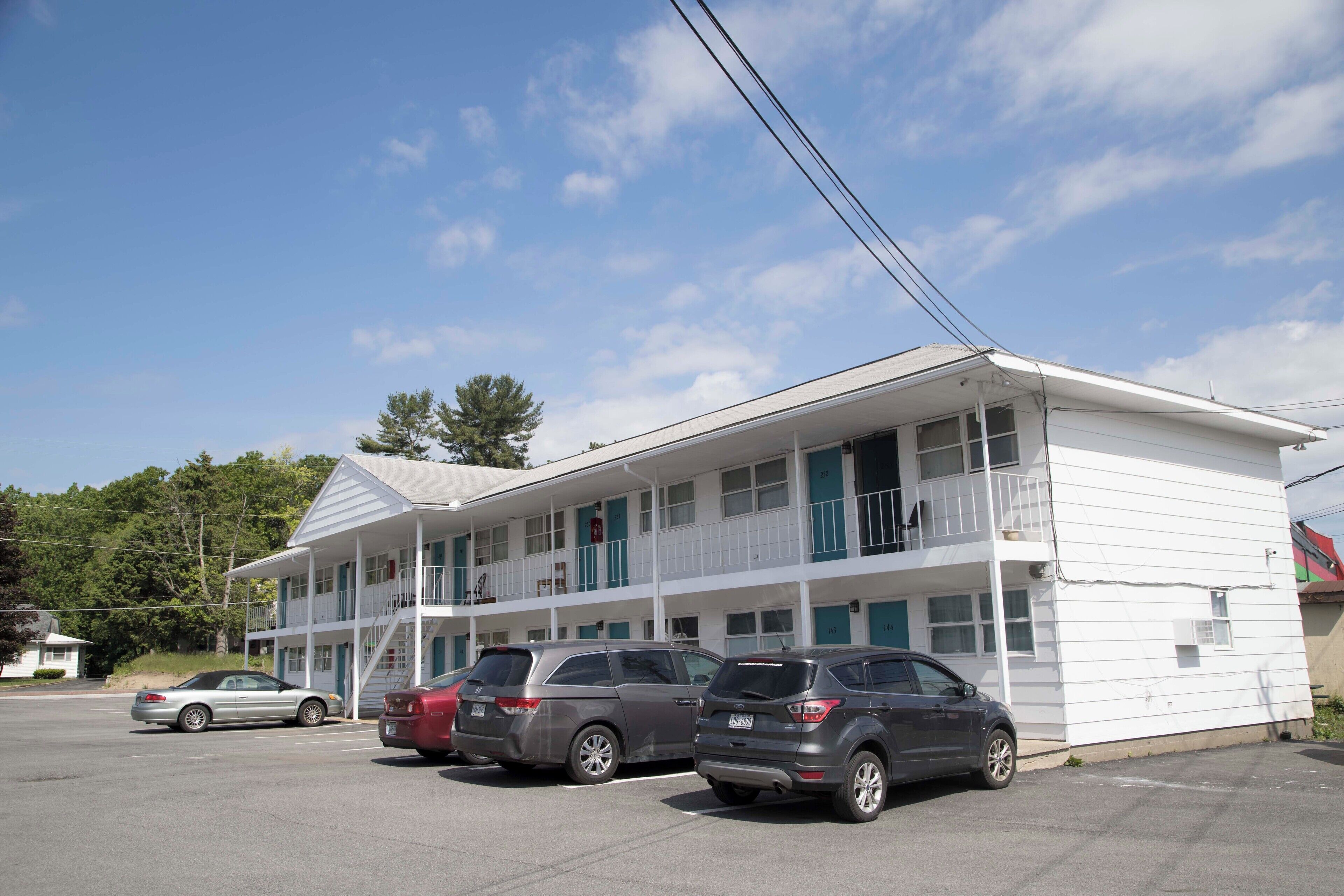 A motel with a two-story structure, multiple balconies, and a parking lot with several cars.