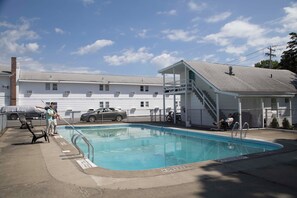 A swimming pool with a covered area, a car, and a building in the background.