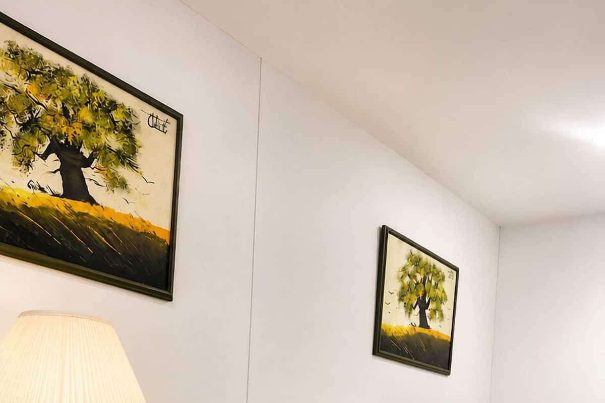 Quarto de hotel bem arrumado, com uma cama, mesa de cabeceira, abajur e duas pinturas emolduradas na parede.