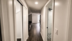 A narrow hallway with a wooden floor, white walls, and a glass shower door. - Lake George Residence LLC (South Glens Falls)