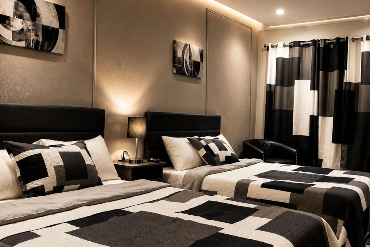 Quarto de hotel com duas camas, uma mesa de cabeceira, uma luminária e uma obra de arte pendurada na parede.